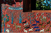 Wat Xieng Thong temple in Luang Prabang, Laos.  La Chapelle Rouge , the Red Chapel. The exterior walls are decorated with colourful mosaics on a pink background with scenes of people daily activities. South wall. 